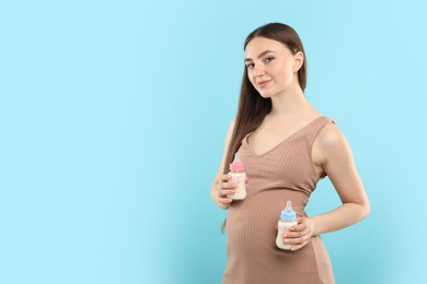 Expecting twins. Pregnant woman holding two bottles with milk on light blue background, space for text