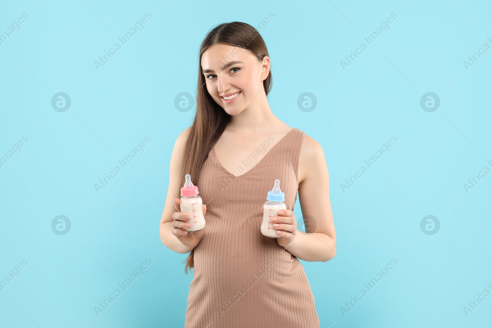 Photo of Expecting twins. Pregnant woman holding two bottles with milk on light blue background