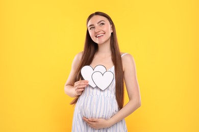 Expecting twins. Pregnant woman holding two paper cutouts of hearts on yellow background