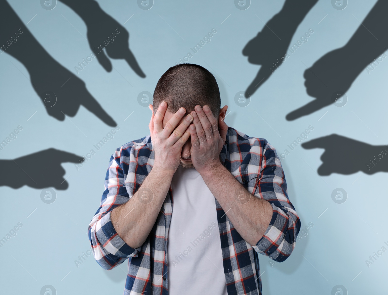 Image of Silhouettes of people's hands pointing at upset man on light blue background. Social pressure, failure, responsibility