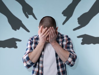 Silhouettes of people's hands pointing at upset man on light blue background. Social pressure, failure, responsibility