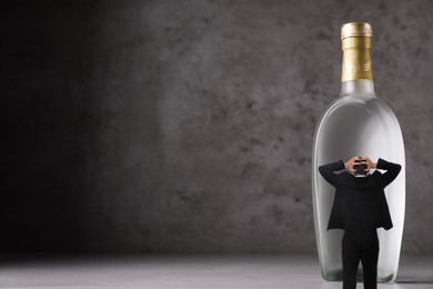 Worried man standing in front of huge bottle of vodka on grey background, space for text. Alcohol addiction concept