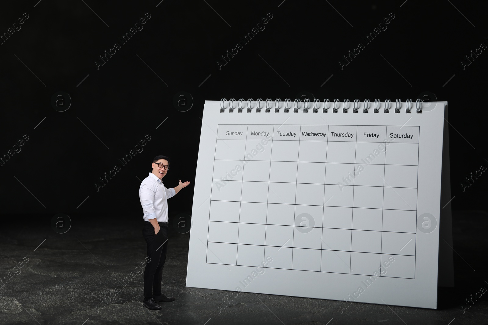 Image of Happy small businessman pointing at big calendar on black background. Concepts of self-management, planning