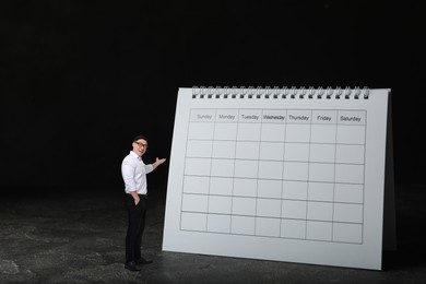 Image of Happy small businessman pointing at big calendar on black background. Concepts of self-management, planning