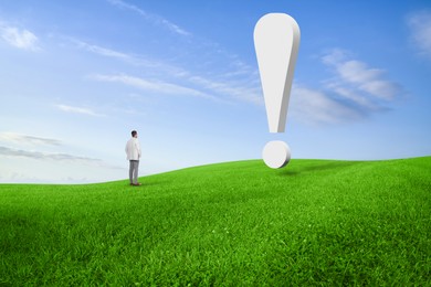 Small businessman looking at huge exclamation mark on green meadow. Concepts of achievement, startup, targeting