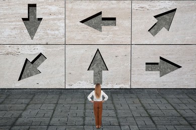 Image of Small businesswoman looking at wall with arrows pointing in different directions. Concept of choice