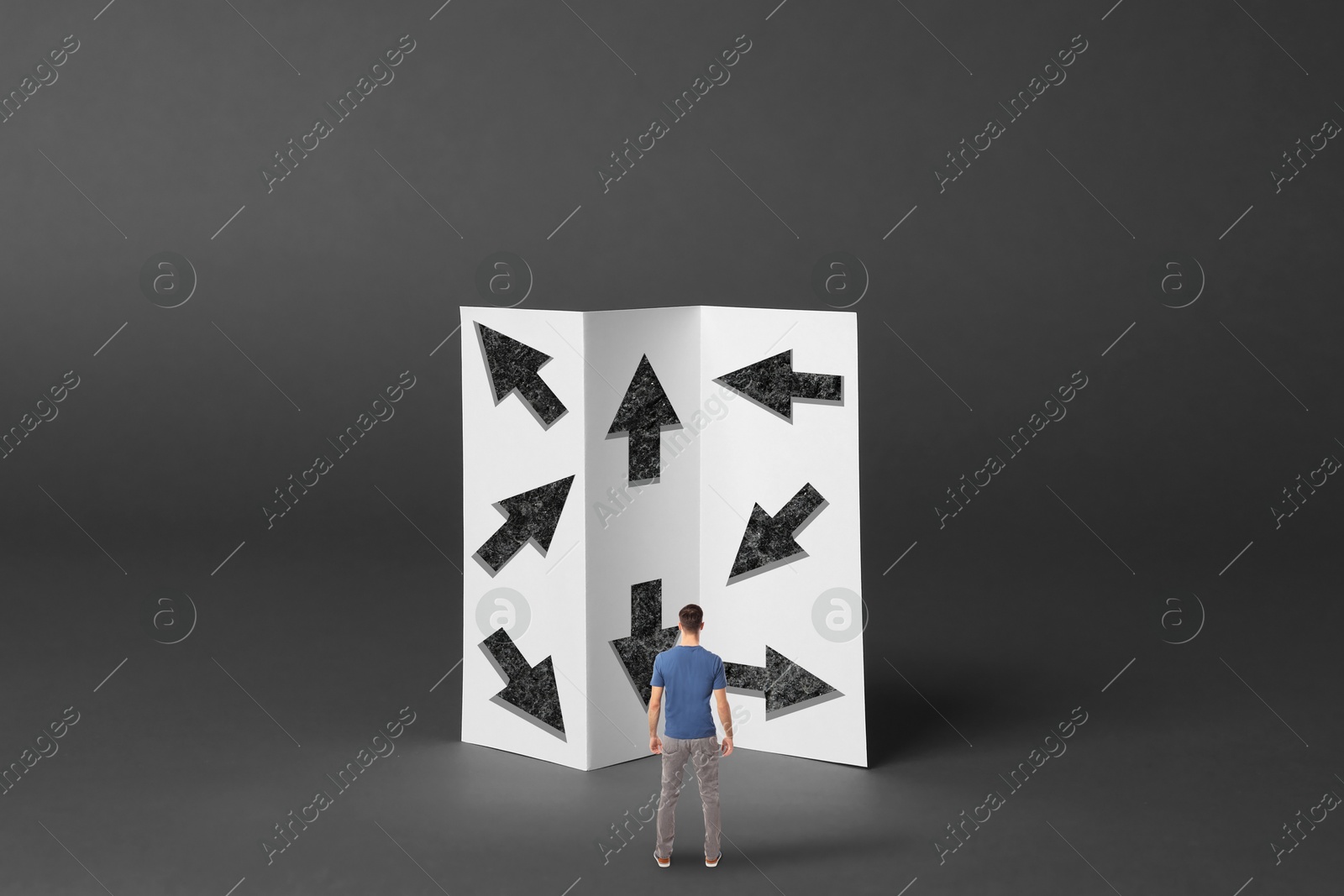 Image of Small man looking at paper with arrows pointing in different directions on grey background. Concept of choice