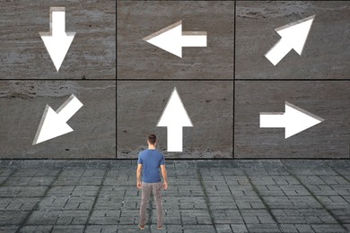 Image of Small man looking at wall with arrows pointing in different directions. Concept of choice