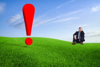 Worried small businessman looking at huge red exclamation mark on green meadow. Concepts of workload, problem