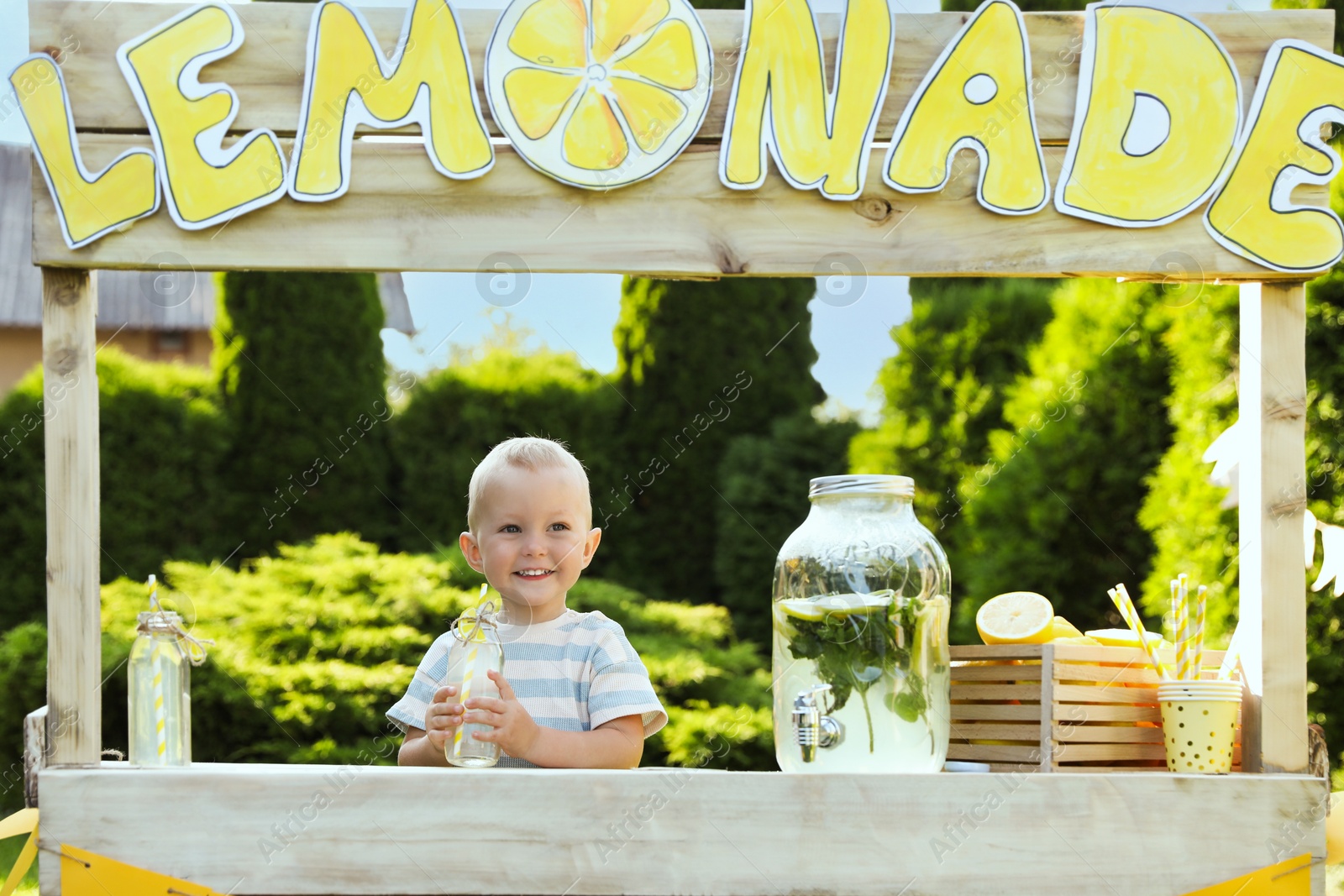 Photo of Cute little boy with refreshing drink at lemonade stand in park