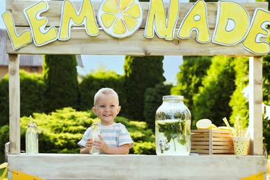 Photo of Cute little boy with refreshing drink at lemonade stand in park