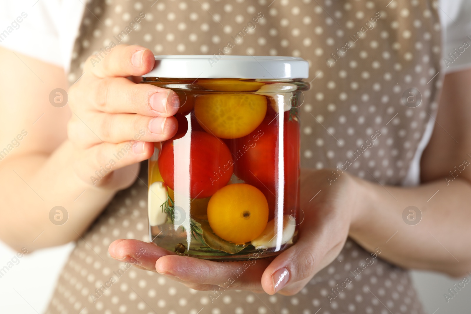 Photo of Woman with jar of tasty pickled tomatoes on light background, closeup