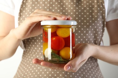 Photo of Woman with jar of tasty pickled tomatoes on light background, closeup