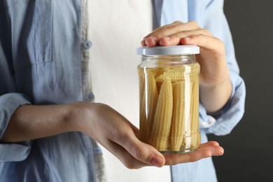 Photo of Woman with jar of tasty pickled yellow baby corns on gray background, closeup