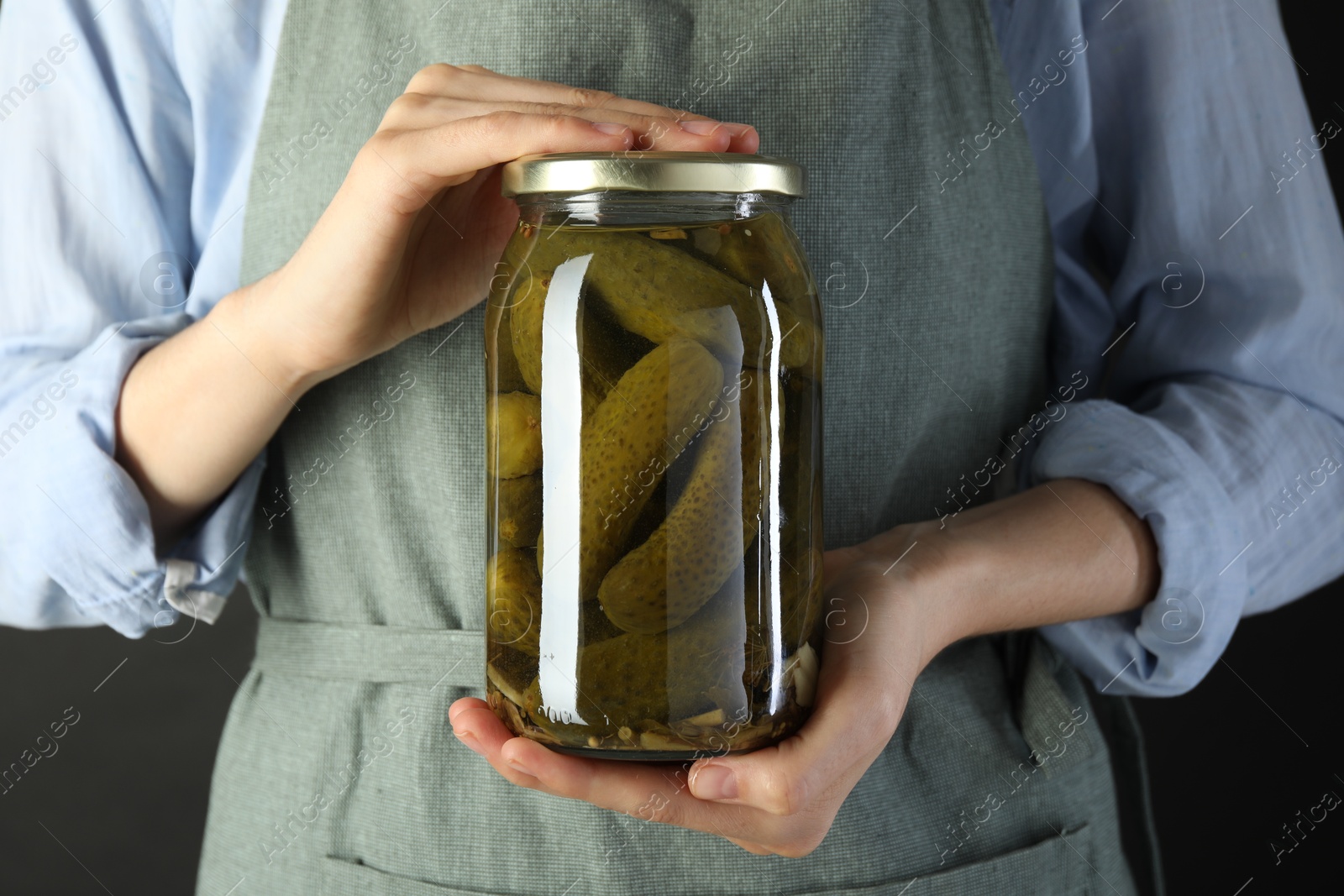 Photo of Woman with jar of tasty pickled cucumbers on gray background, closeup