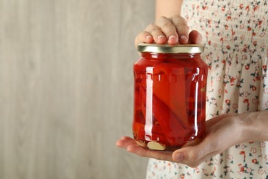 Photo of Woman with jar of tasty pickled peppers indoors, closeup. Space for text