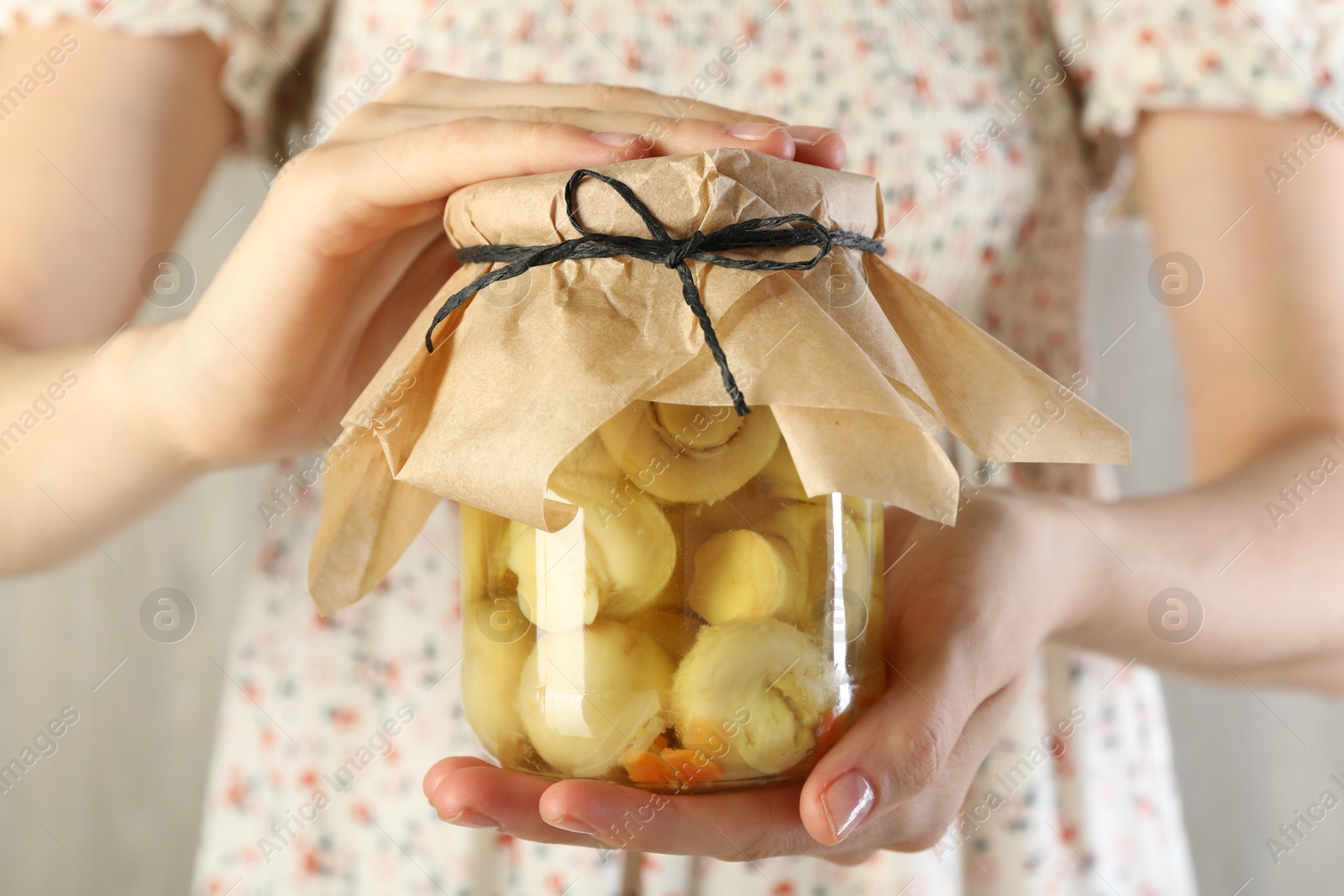 Photo of Woman with jar of tasty pickled mushrooms on light background, closeup