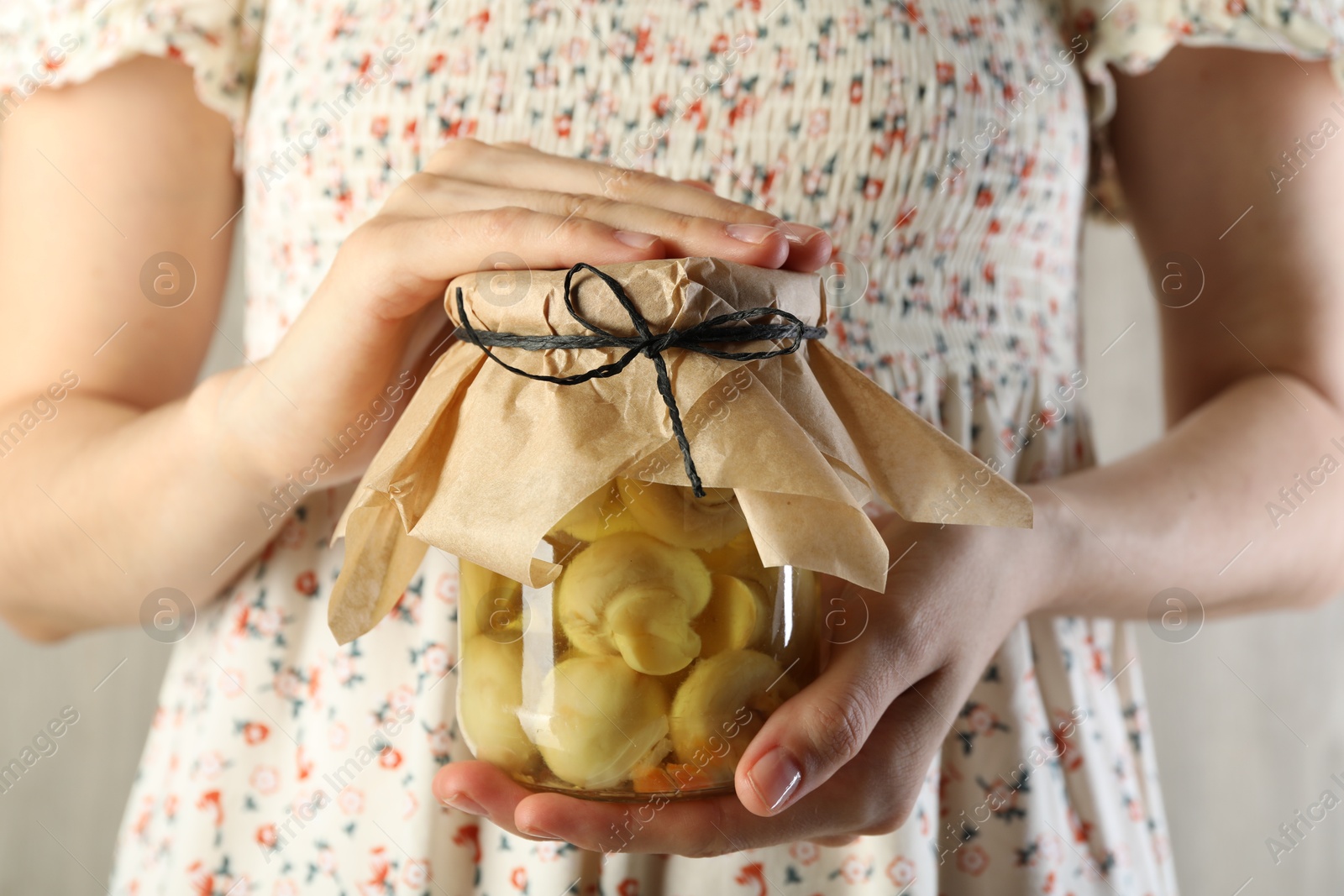 Photo of Woman with jar of tasty pickled mushrooms on light background, closeup