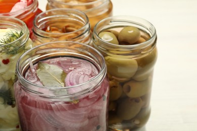 Photo of Different pickled products in jars on light table, closeup