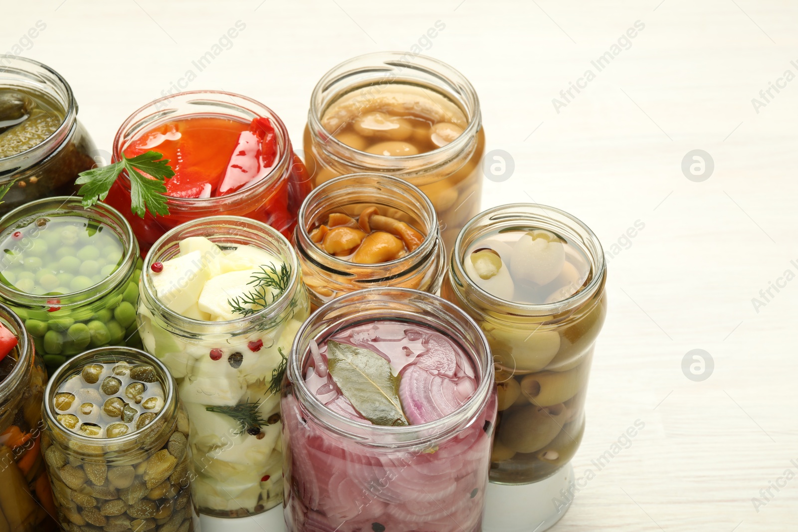 Photo of Different pickled products in jars on light table, closeup