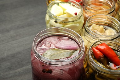 Photo of Different pickled products in jars on dark wooden table, closeup