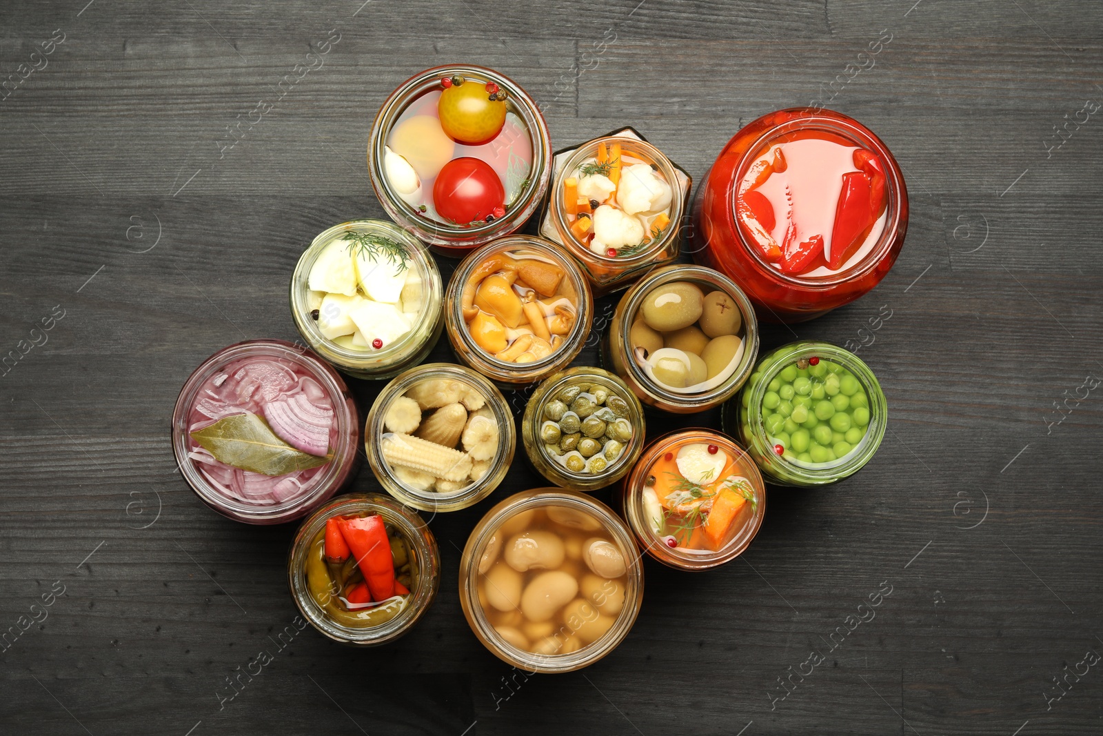 Photo of Different pickled products in jars on dark wooden table, top view