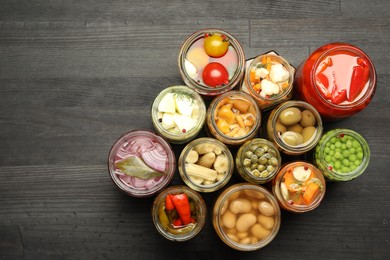 Photo of Different pickled products in jars on dark wooden table, top view. Space for text