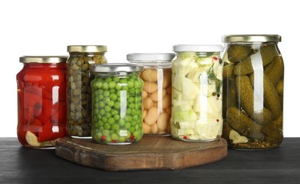 Photo of Different pickled products in jars on dark wooden table against white background