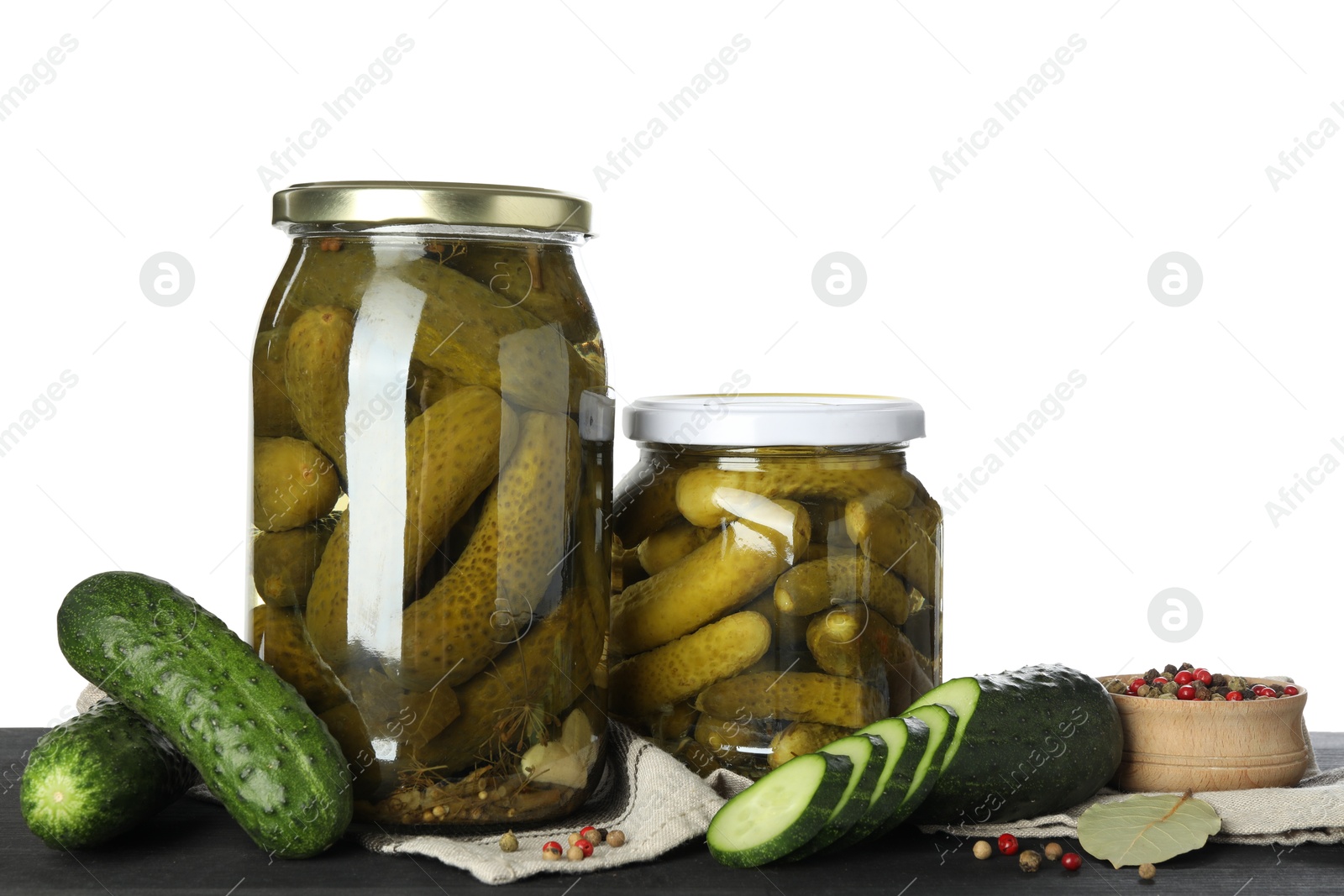 Photo of Tasty pickled cucumbers in jars, fresh vegetables and spices on dark wooden table against white background