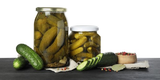 Tasty pickled cucumbers in jars, fresh vegetables and spices on dark wooden table against white background