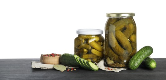 Photo of Tasty pickled cucumbers in jars, fresh vegetables and spices on dark wooden table against white background