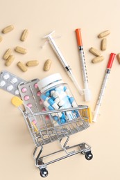 Pharmacist concept. Small shopping cart, syringes and pills on beige background, flat lay