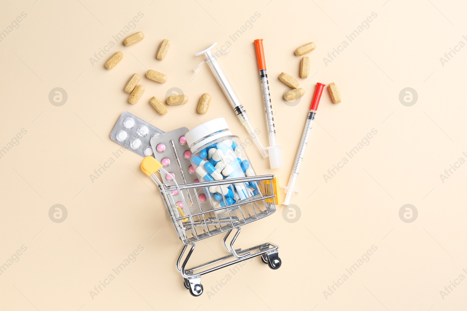 Photo of Pharmacist concept. Small shopping cart, syringes and pills on beige background, flat lay