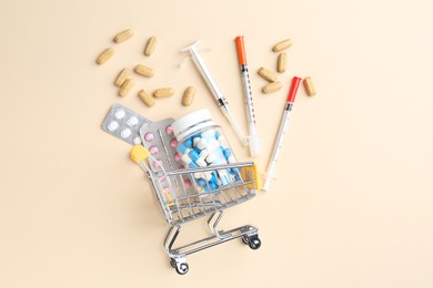 Pharmacist concept. Small shopping cart, syringes and pills on beige background, flat lay