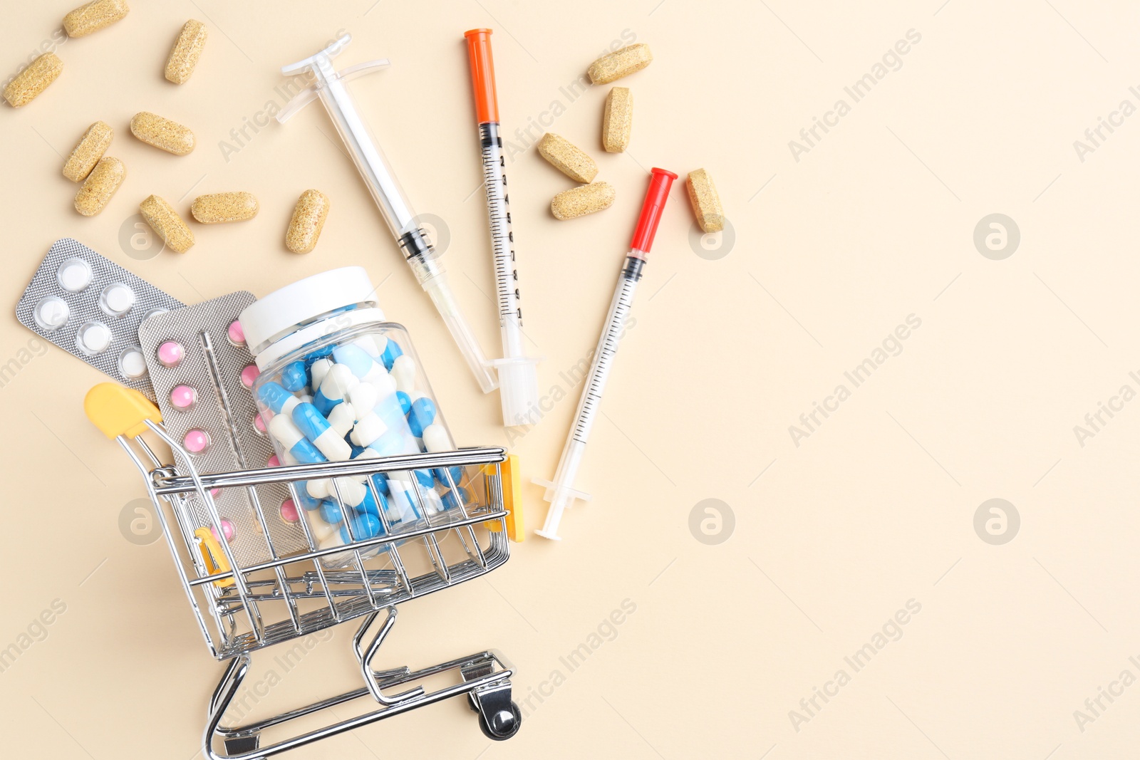 Photo of Pharmacist concept. Small shopping cart, syringes and pills on beige background, flat lay. Space for text