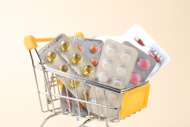 Pharmacist. Many different pills in small shopping cart on beige background, closeup