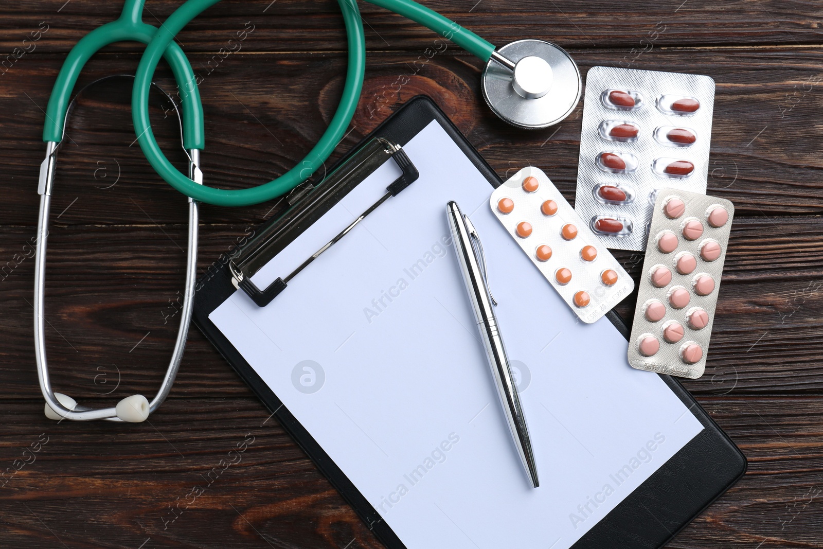 Photo of Pharmacist. Many different pills, clipboard, pen and stethoscope on wooden table, top view