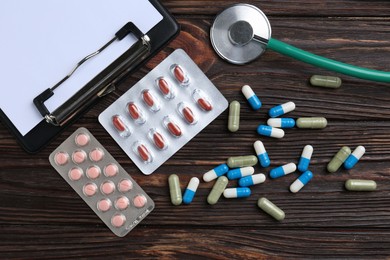 Pharmacist. Many different pills, clipboard and stethoscope on wooden table, flat lay