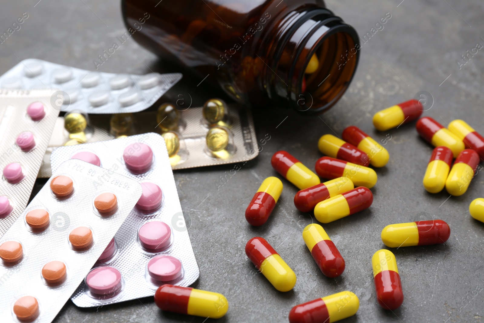 Photo of Pharmacist. Many different pills and overturned bottle on grey table, closeup