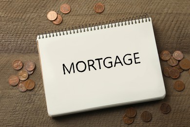 Image of Word Mortgage written in notebook and coins on wooden table, top view