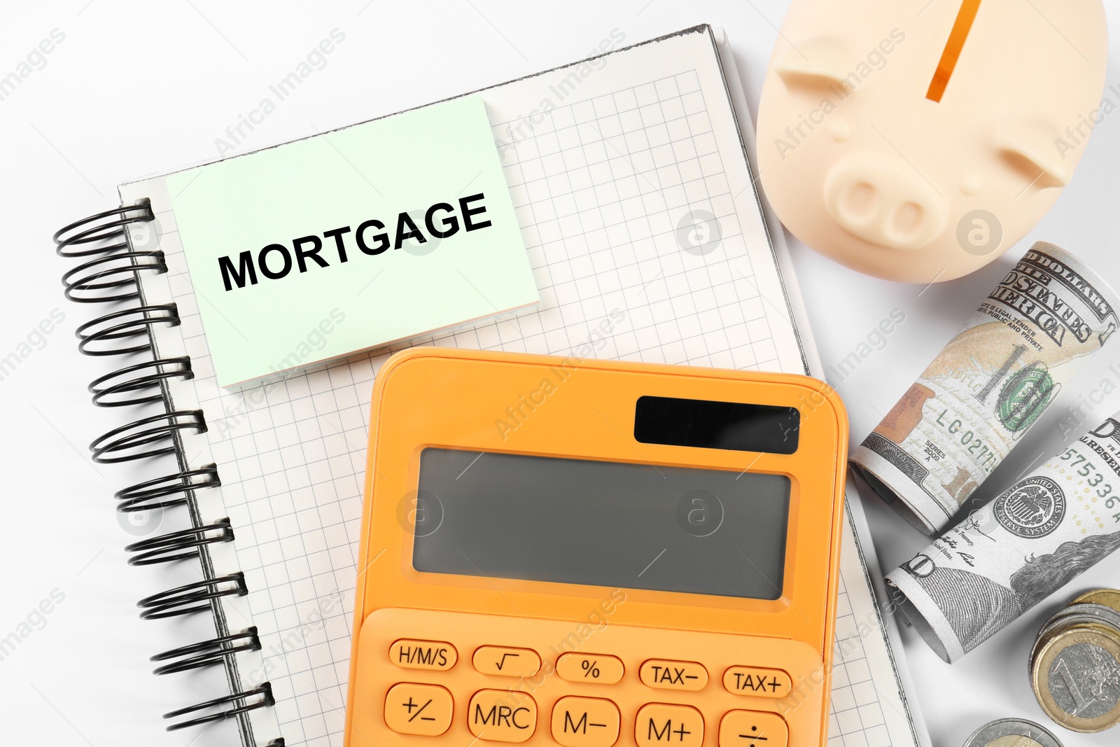 Image of Word Mortgage in notebook, calculator, piggy bank and dollars on white table, flat lay