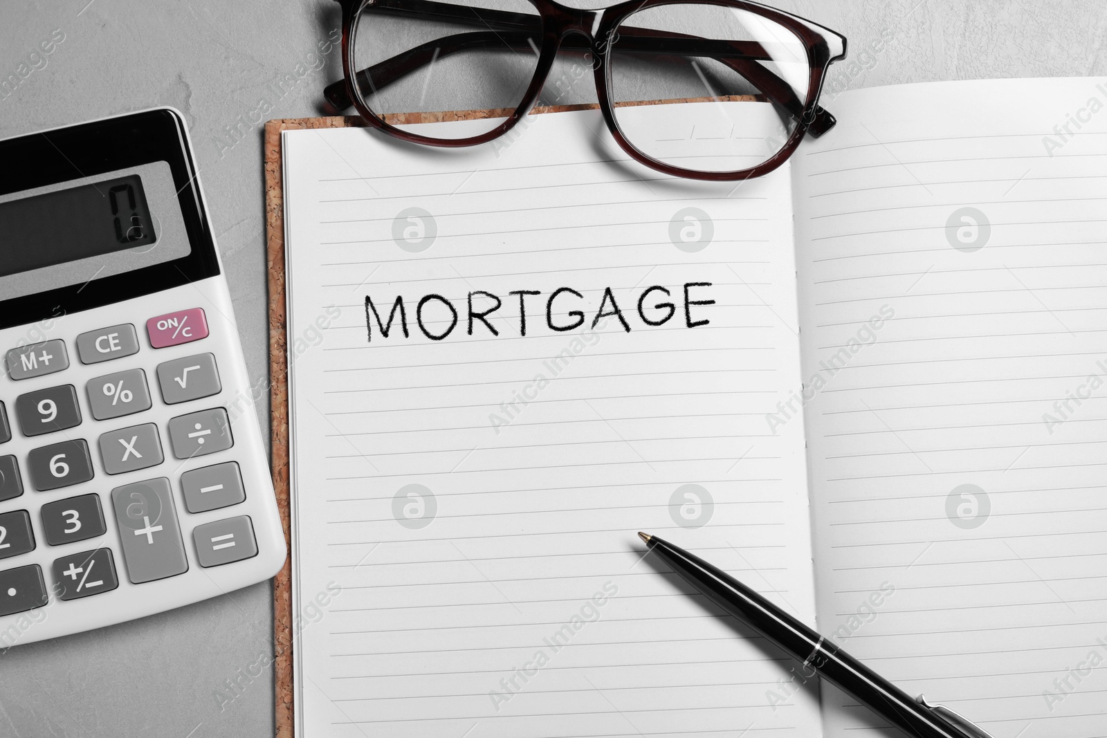 Image of Word Mortgage written in notebook, calculator, eyeglasses and pen on grey table, flat lay