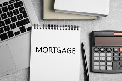 Image of Word Mortgage in notebook, calculator and laptop on grey table, flat lay