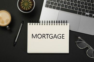 Image of Word Mortgage in notebook, eyeglasses and computer keyboard on black table, flat lay