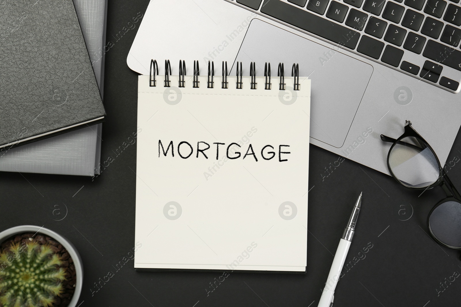 Image of Word Mortgage in notebook, eyeglasses and computer keyboard on black table, flat lay