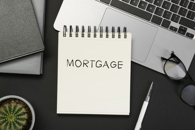 Image of Word Mortgage in notebook, eyeglasses and computer keyboard on black table, flat lay