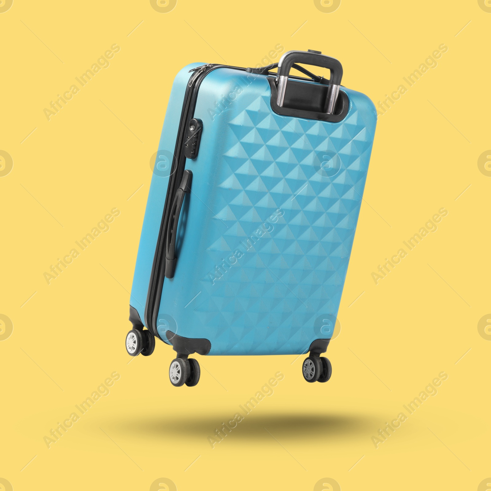 Image of Light blue suitcase in air on yellow background