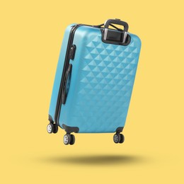 Image of Light blue suitcase in air on yellow background