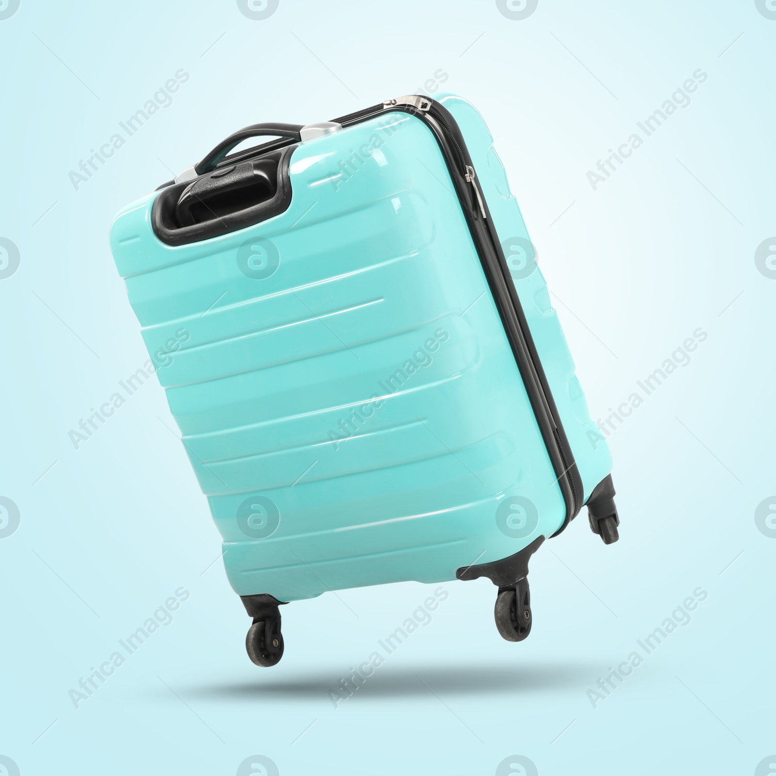 Image of Turquoise suitcase in air on light blue background