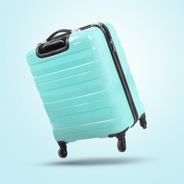 Image of Turquoise suitcase in air on light blue background